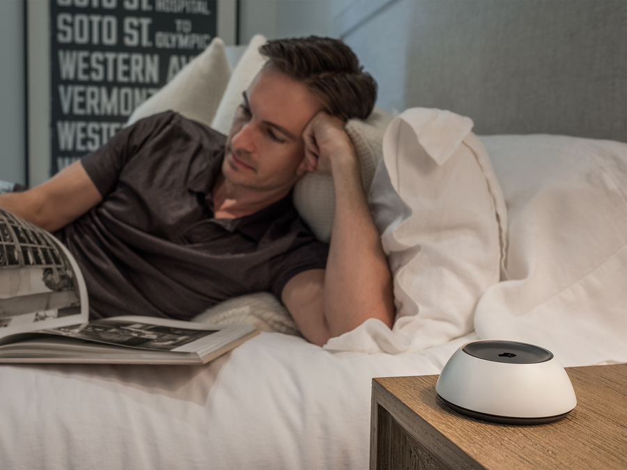 Man reading in bed with a Josh.ai home voice control device on the bedside table.